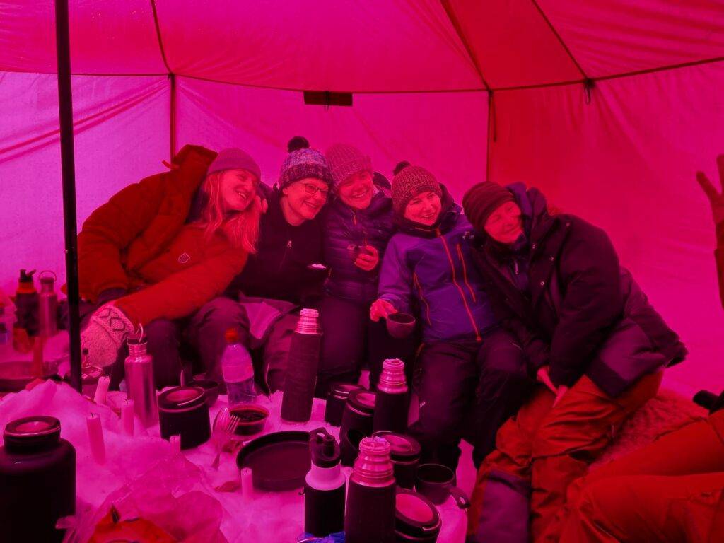 5 women in a tent eating food in the off piste camp. Very cold temperatures.