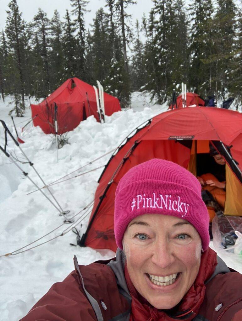 woman infront of red tent in a campsite in a swedish forest. Fulfulling a dream to live off-grid and off-piste
