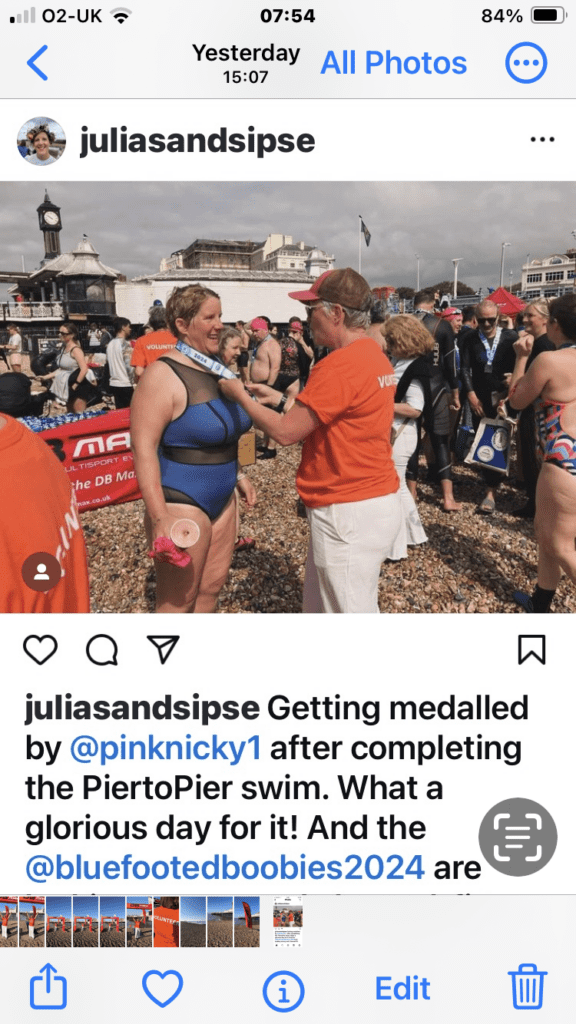 1 volunteer putting a medal around the neck of a swimmer wavin on the finish line at the Brighton Pier to Pier Sea swim. The Benefits of Volunteering: why helping others is good for you!