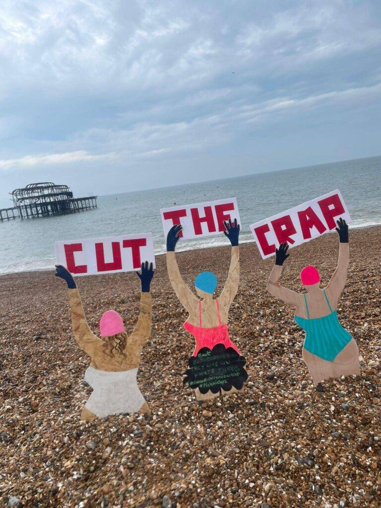 3 wooden models holding sign saying cut the crap - supporting surfers against sewage clean water campaign