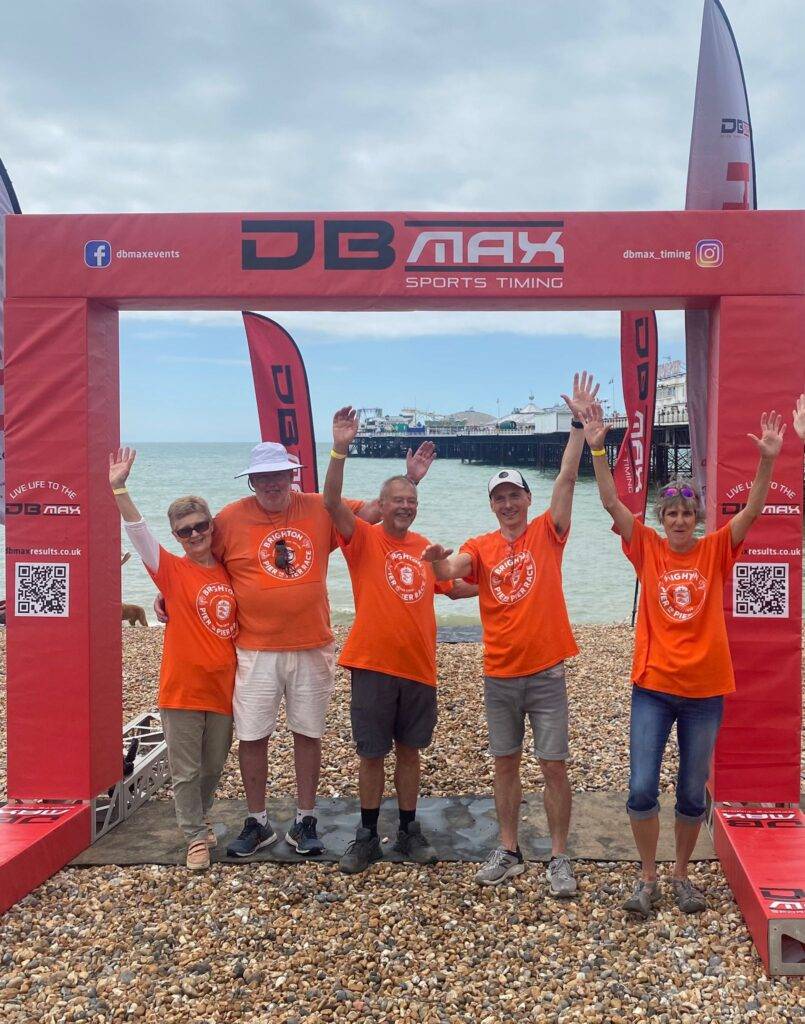 5 volunteers waving on the finish line at the Brighton Pier to Pier Sea swim. The Benefits of Volunteering: why helping others is good for you!