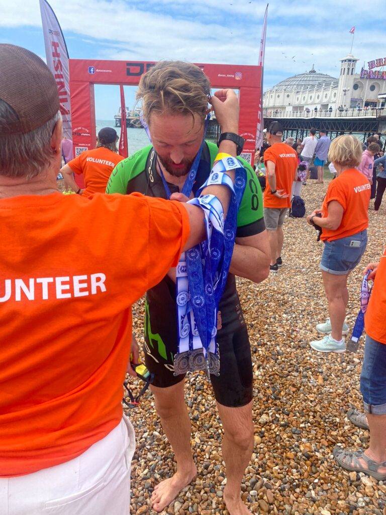 1 volunteer handing over a medal to a swimmer at the finish line at the Brighton Pier to Pier Sea swim. The Benefits of Volunteering: why helping others is good for you!